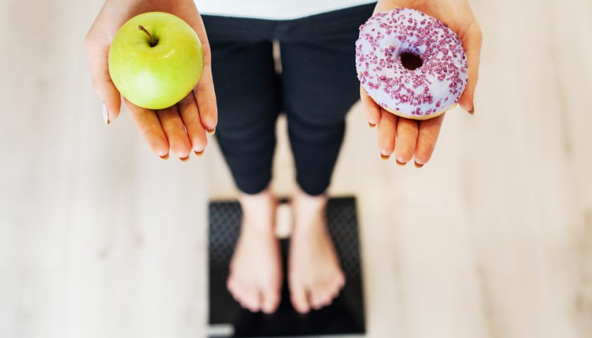 femme sur une balance avec une pomme et donut dans les mains